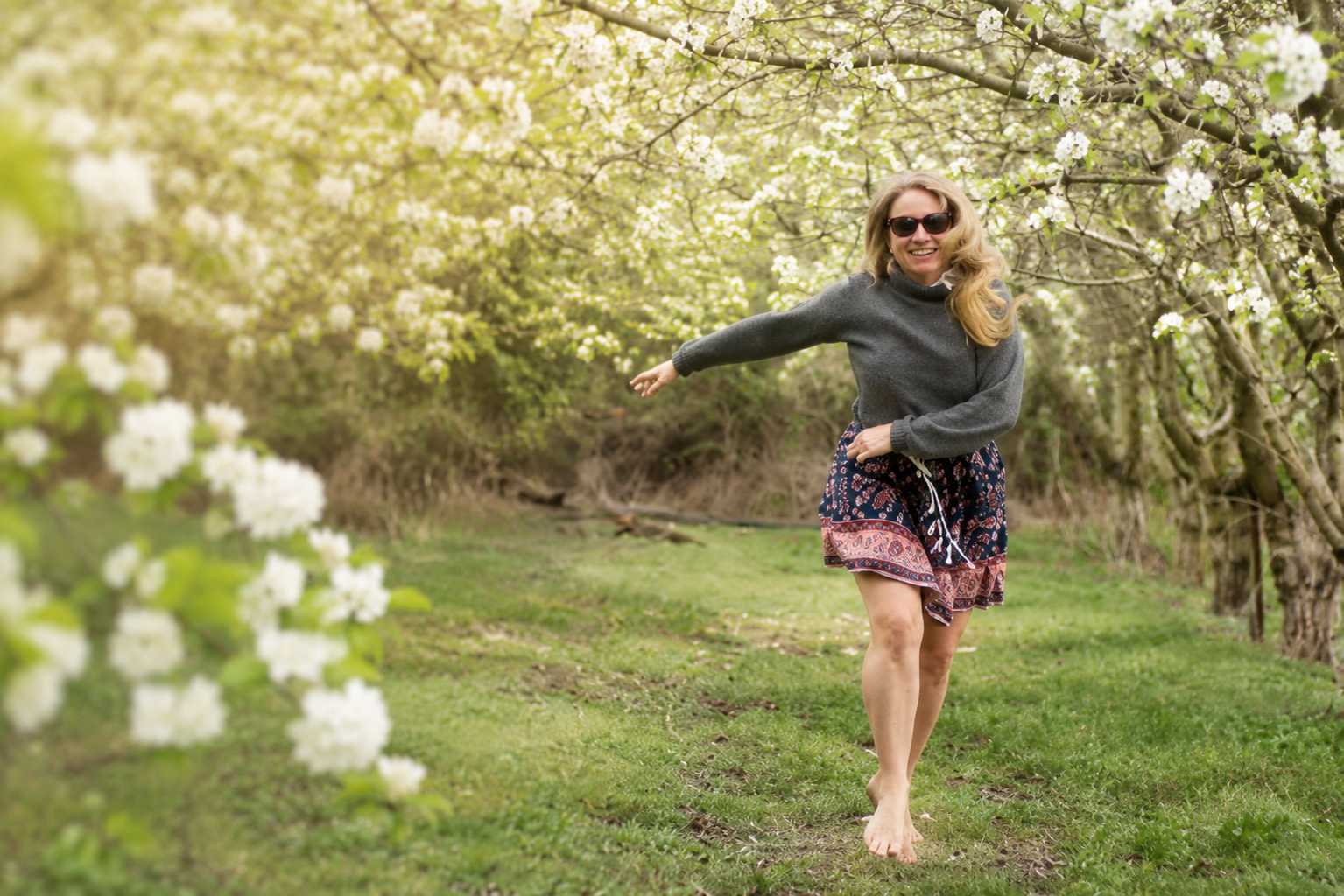 Woman running through blooming pear trees in spring resembling snowflakes, symbolising letting go of the past and embracing new joy in Cyprus